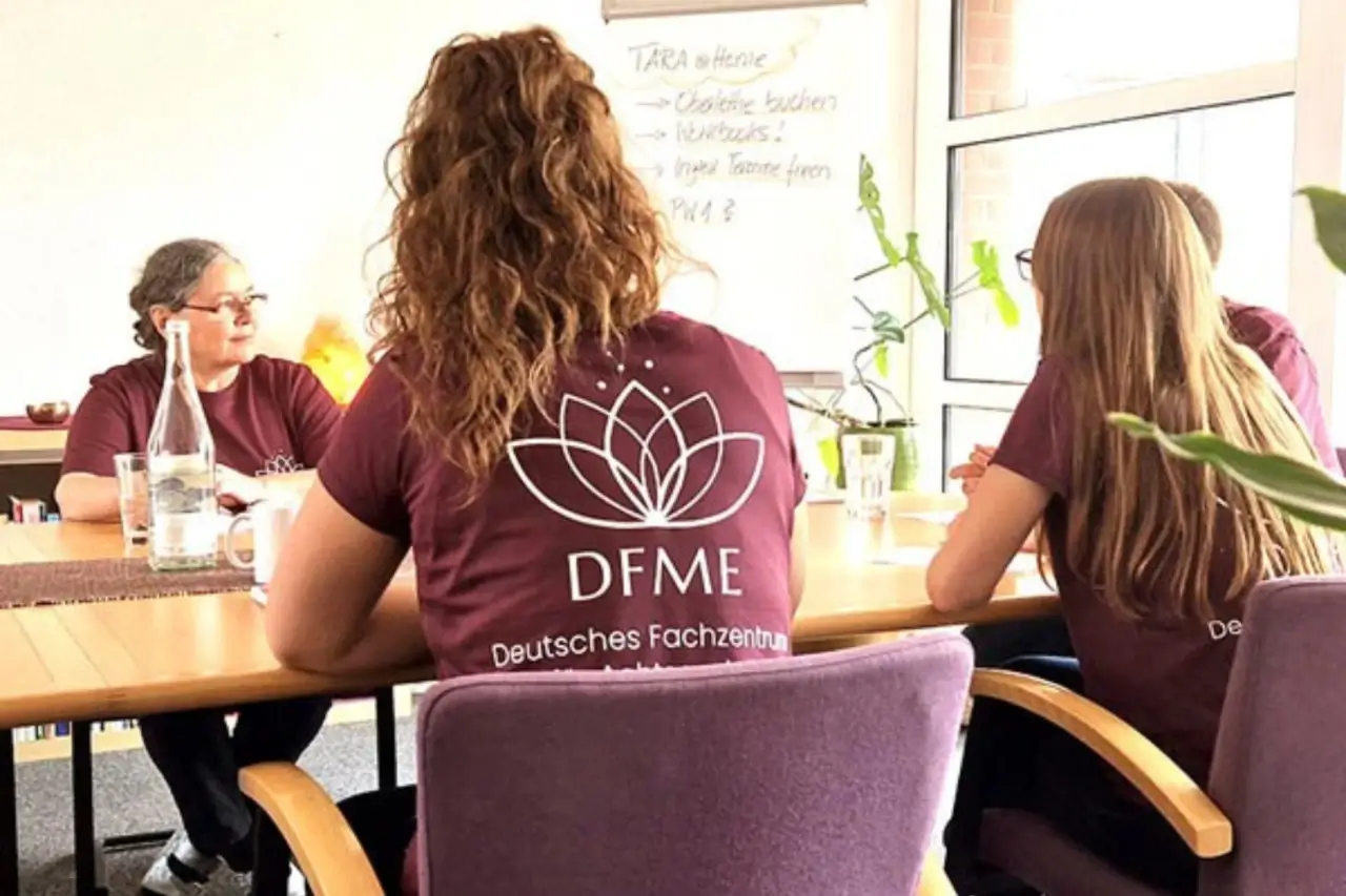 Eine Gruppe Menschen sitzt in heller Atmosphäre um einen Tisch, sie tragen T-Shirts des DFME