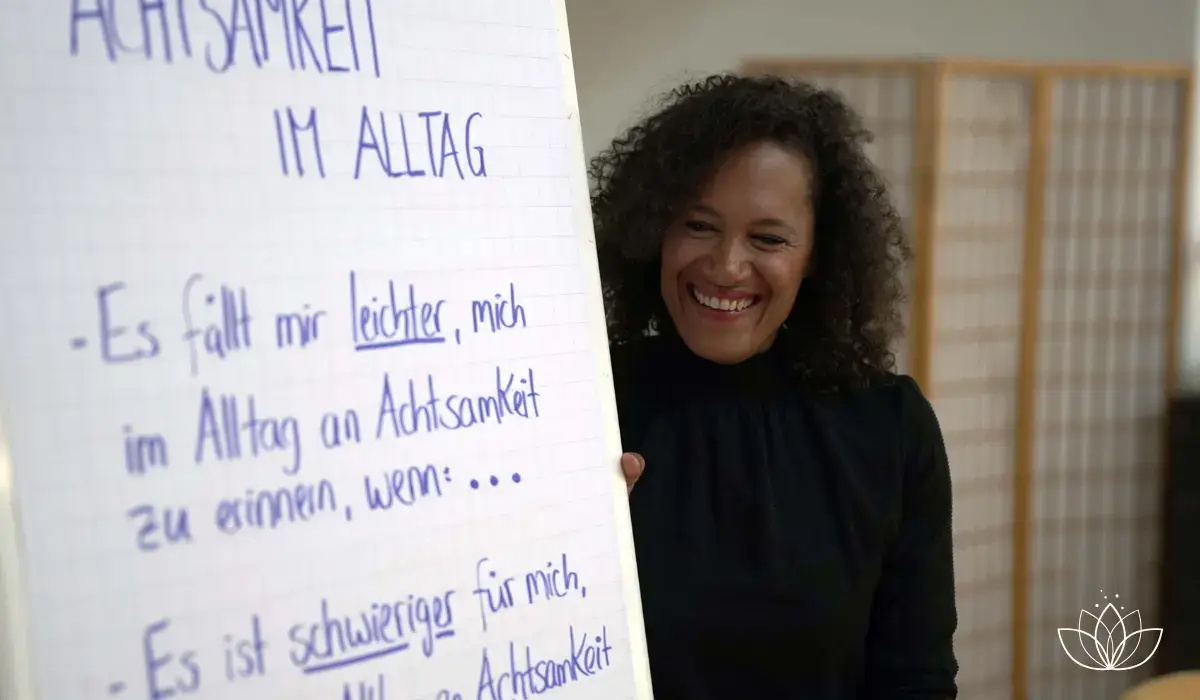 Lachende Achtsamkeitstrainerin neben einem Flipchart mit der Aufschrift Achtsamkeit im Alltag